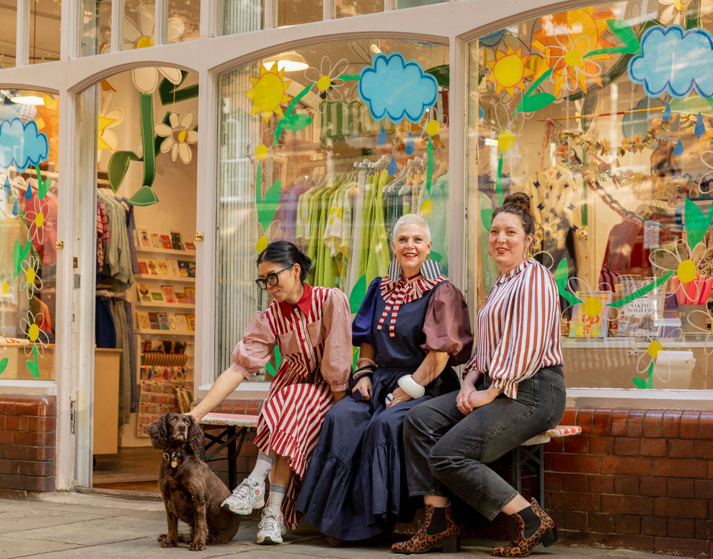 Three women sitting on a bench in front of an independent  store in Shoreditch with colorful window displays.