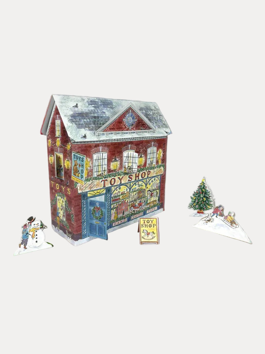 A fold-out advent calendar depicting a toy shop with a red facade, illustrated by Emily Sutton. The shop is adorned with Christmas decorations, and the calendar includes small figures of people and a dog outside the shop.